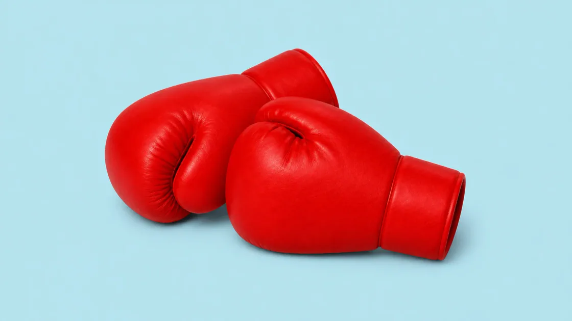Original wide studio image of two red boxing gloves resting together on pale blue